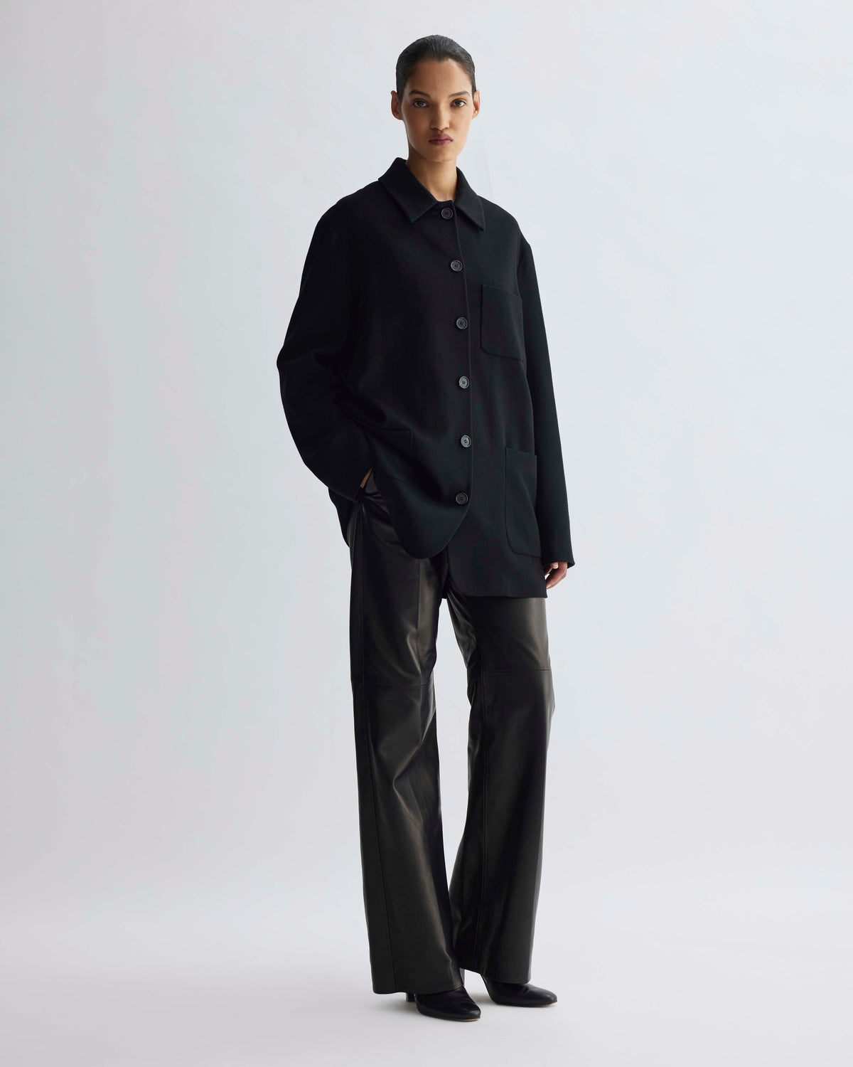 Black oversized structured wool shirt jacket with button front, patch pockets, styled with black wide-leg leather pants