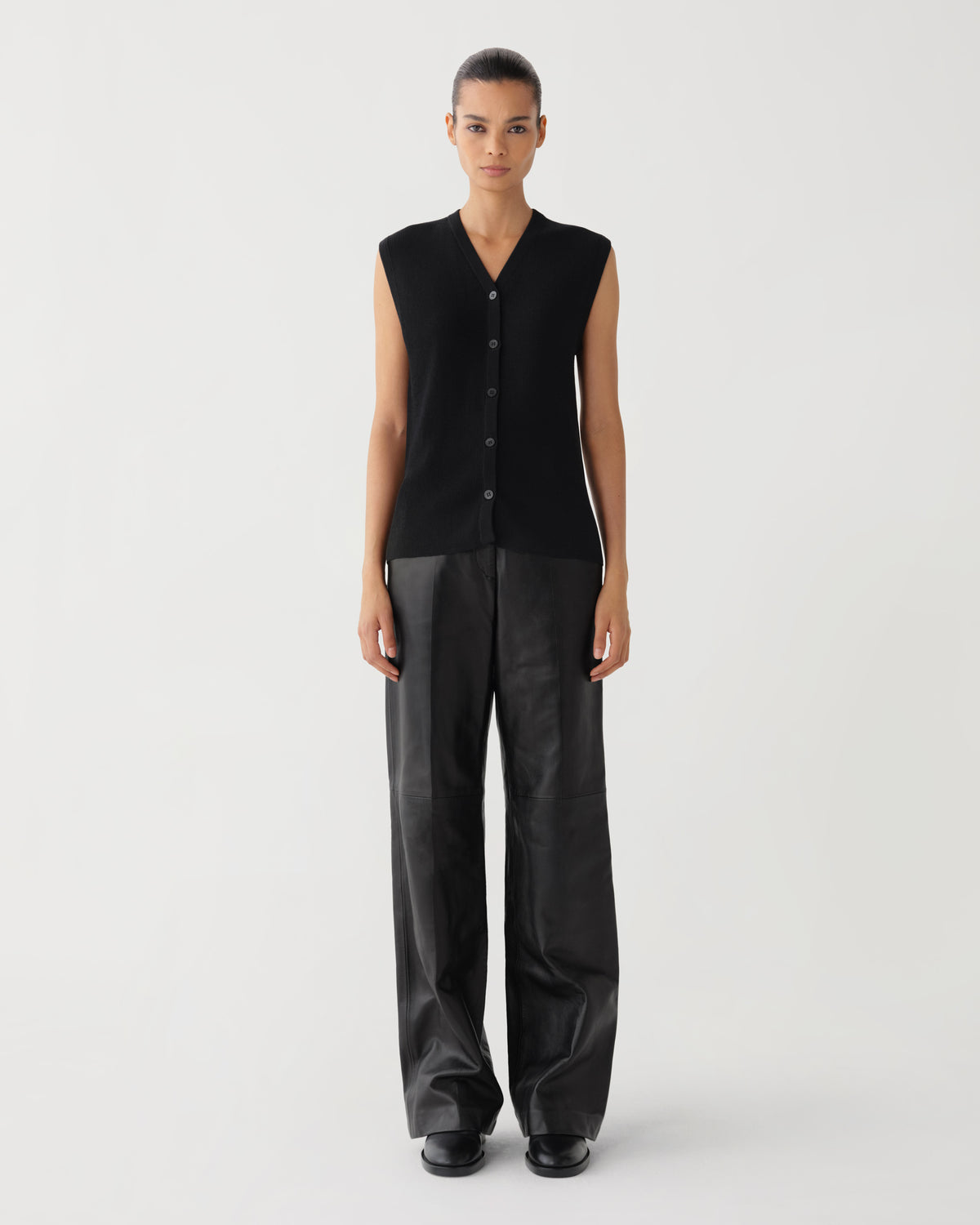 Women's black ribbed knit V-neck sleeveless top and wide-leg black leather trousers on a model