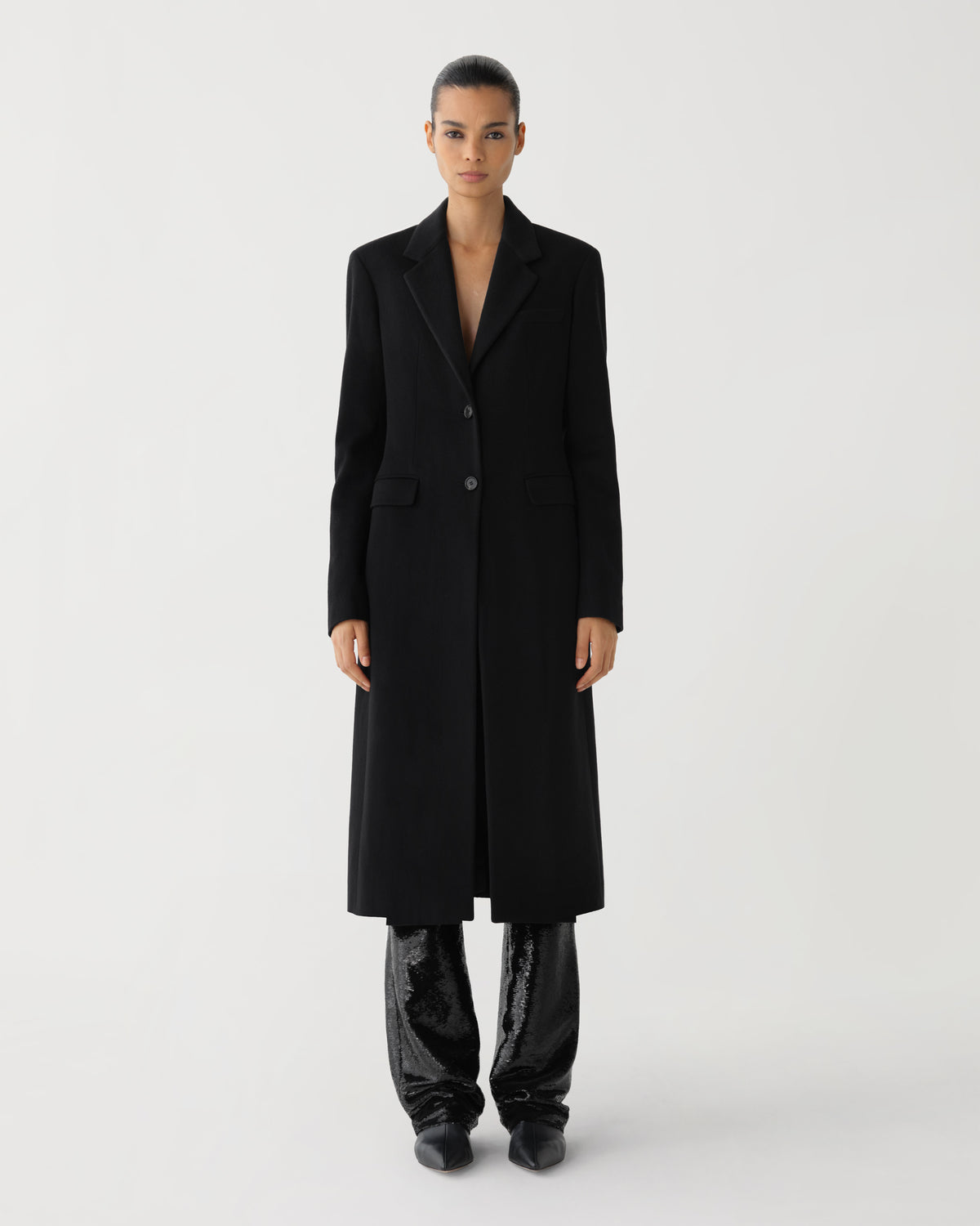 Black wool longline single-breasted coat with notched lapels, paired with sparkling black sequin trousers on a female model
