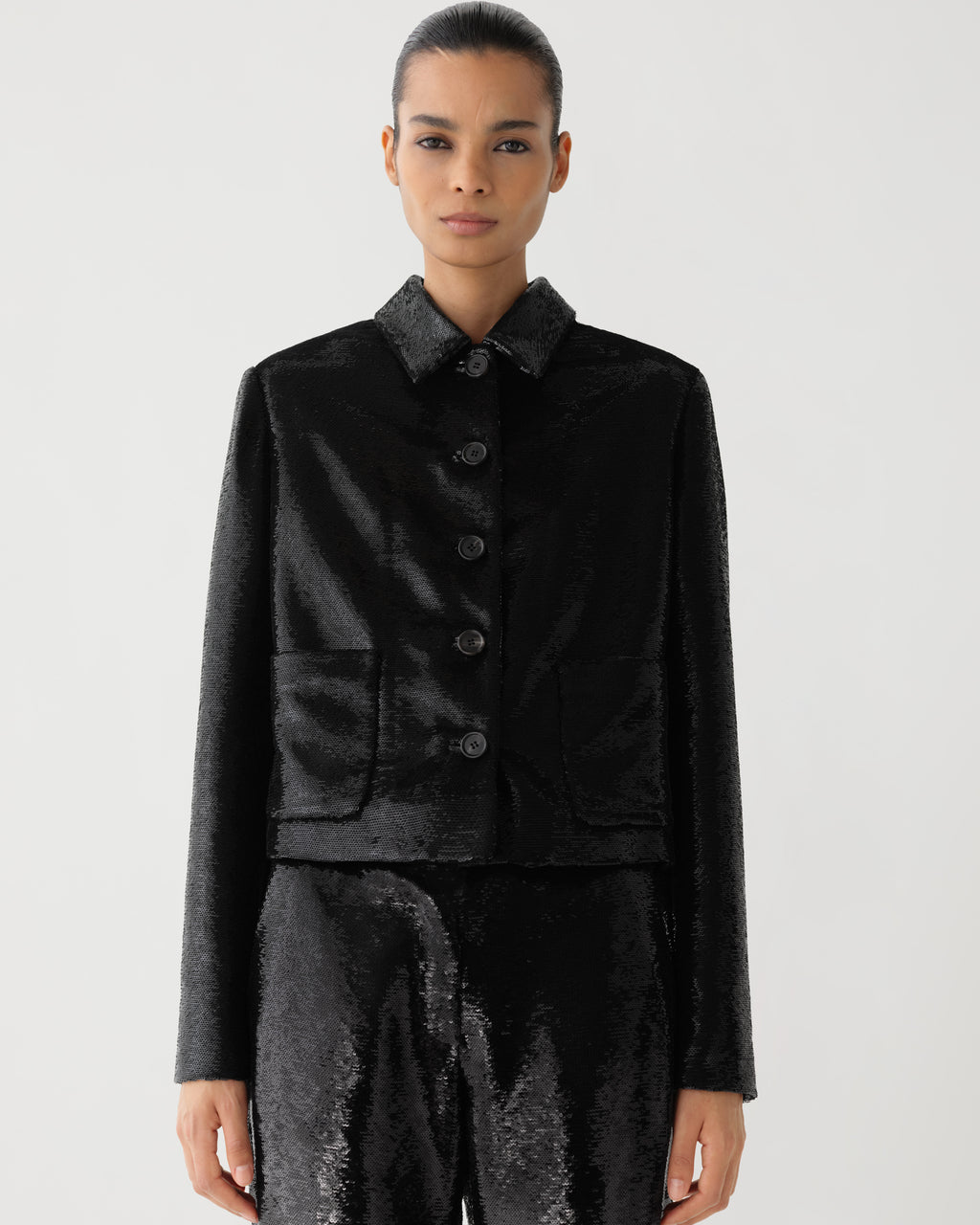 Black Ines Jacket in flat sequins by Veronica De Piante, shown on a hanger with close-up of its shimmering sequin details.