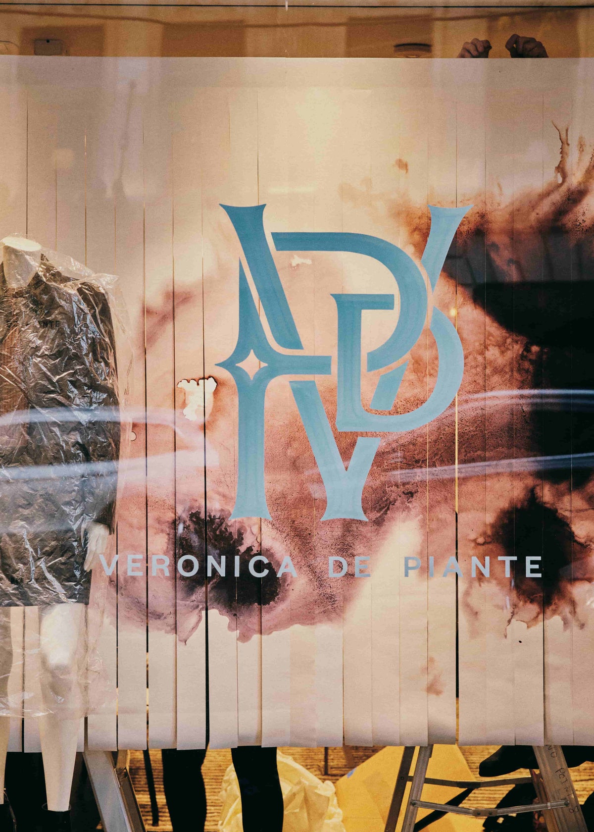 Veronica de Piante boutique window display Stylized blue VDP logo abstract textured brown-black background dark garment