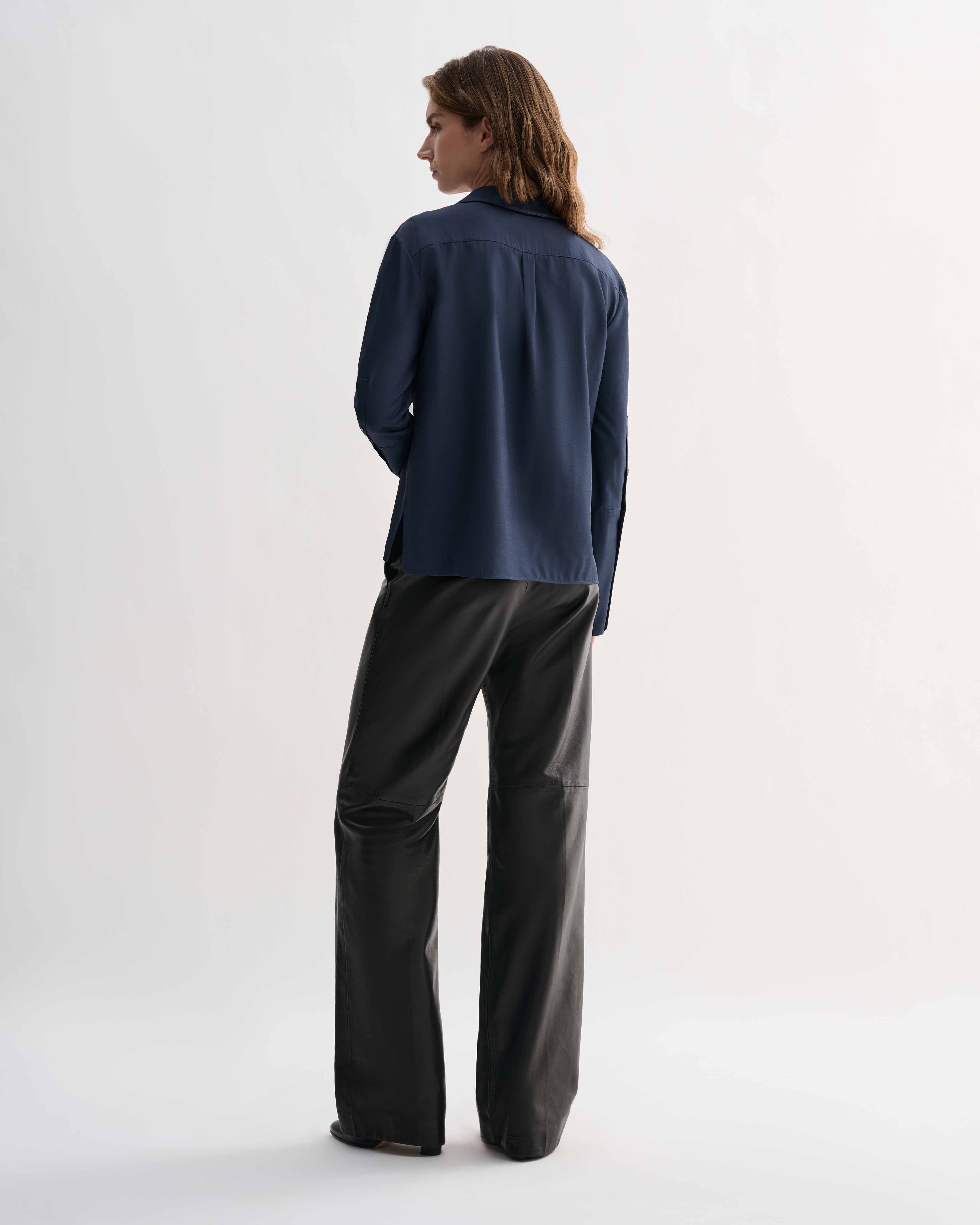 Livia Silk Shirt, Petrol Blue, back view on model. Feminine long-sleeve button-up top with elongated cuffs