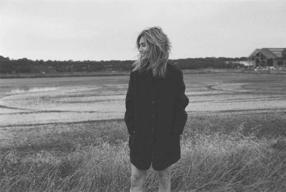 Dark oversized wool-blend coat, relaxed fit, knee-length, hands in pockets, model in outdoor field setting