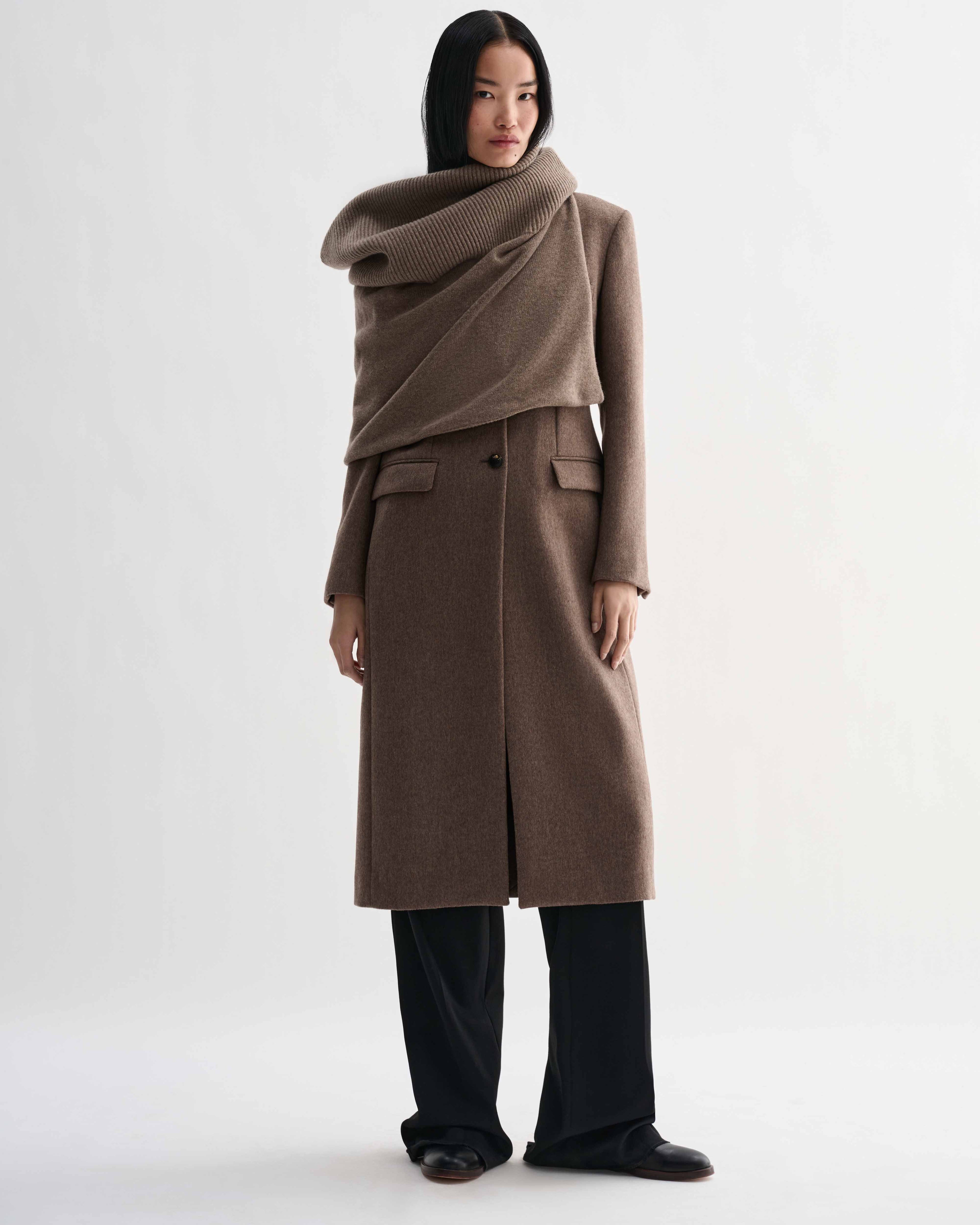 Camel wool cashmere Caro Snood knitwear on model. Dense gauge knitted shawl, generously draped over shoulders.