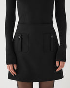 Black Sabine skirt in stretch wool twill by Veronica De Piante, shown on a hanger with a close-up of the fabric texture.