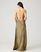 A woman shown from the back wearing a floor-length leopard-print slip dress with thin crisscross straps and an open back, photographed against a light gray studio background.