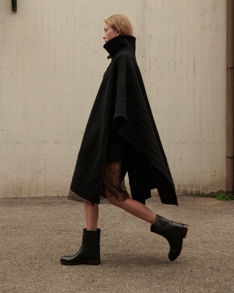 Black luxury wool blend cape with high stand collar, ribbed details, worn over black lace dress and leather ankle boots