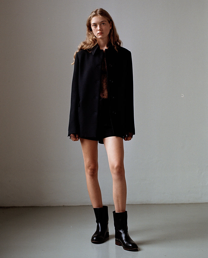 Black oversized wool blend blazer, sheer lace top, tailored shorts, and black leather ankle boots on a female model