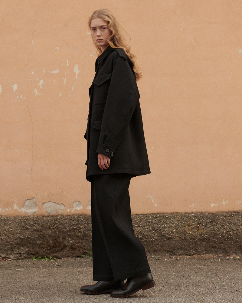 Women's black oversized wool blend utility jacket with flap pockets, black wide leg trousers, and dark leather ankle boots
