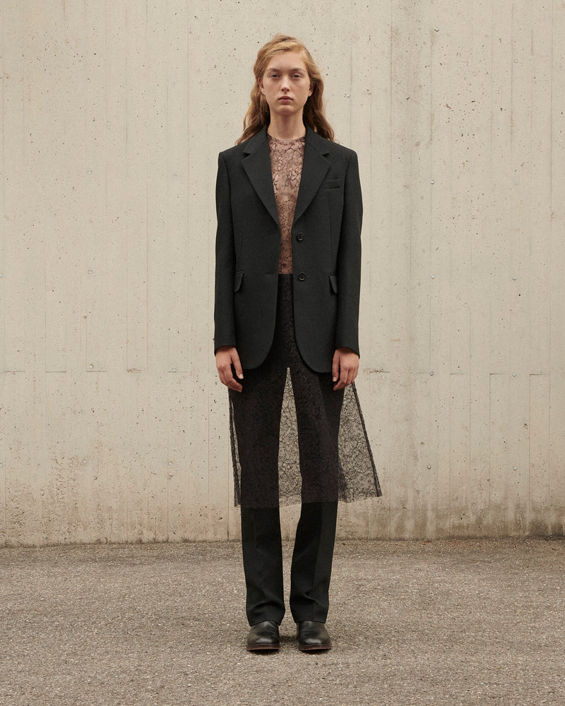 Woman in black tailored wool blazer, nude floral lace blouse, black straight trousers, and sheer embroidered lace overlay
