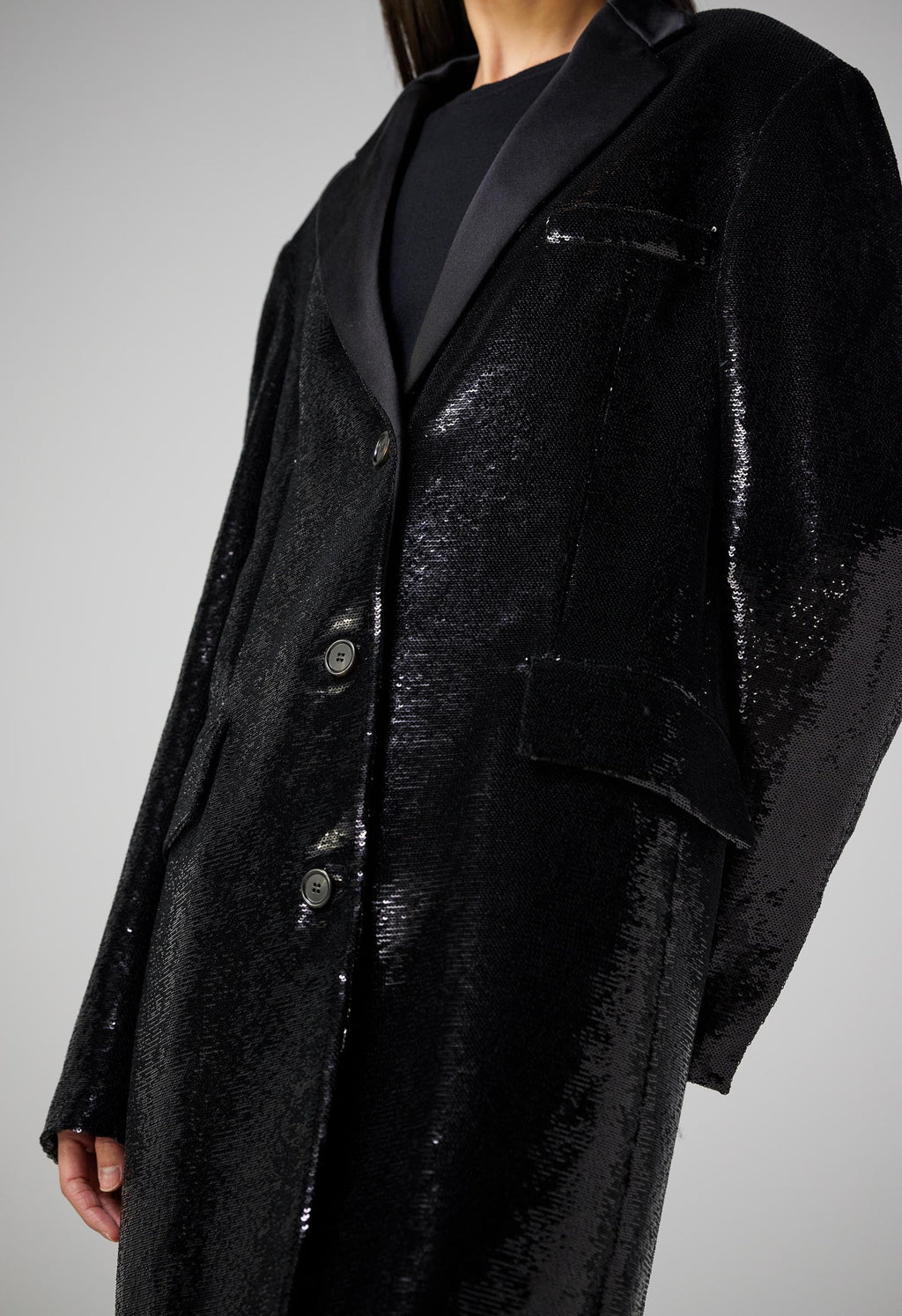 Black flat sequin Arlo coat by SALE, showcasing a sleek design and elegant texture in a stylish outdoor setting.